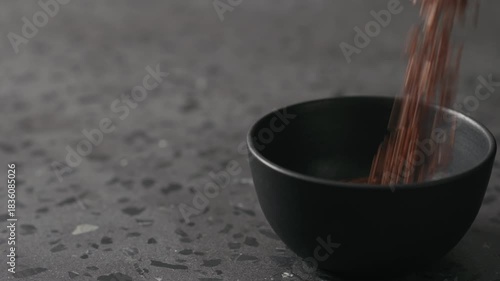 Slow motion flaxseed falling into black bowl on terrazzo countertop