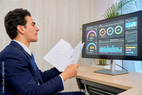 Businessman checking document paper to analyst data with monitor information in co-working space working.