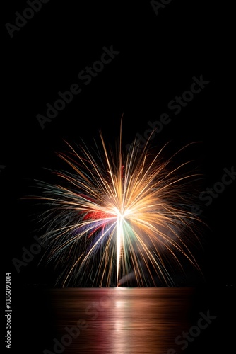 Fireworks display illuminates the night sky with vibrant colors and dazzling light show above water
