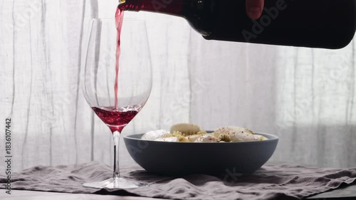 Slow motion pour red wine into wineglass with pasta on background