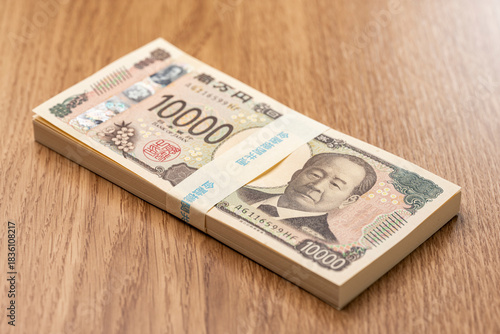 木目テーブルに置かれた百万円の一万円札束が象徴する日本円の高額資金