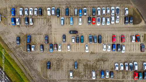 Aerial view of a crowded parking lot with parked cars, marked spaces, winter pavement texture and a parallel layout of parking rows