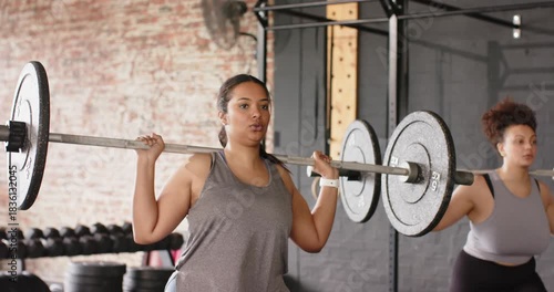 Upon barbell settling, diverse female friends bracing cores, squatting to tone legs by squat rack