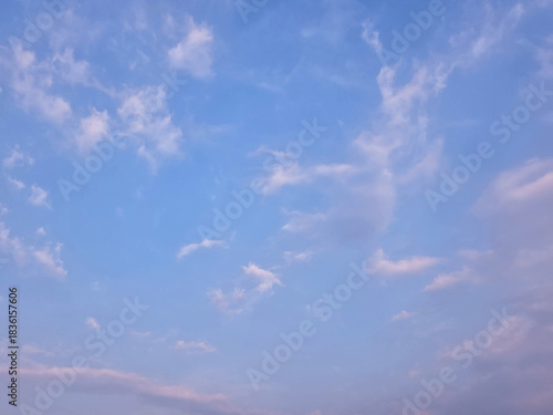 Soft pastel blue sky with gentle scattered clouds drifting across the horizon on a calm summer afternoon