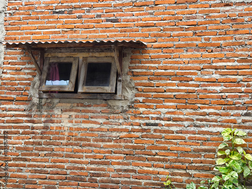Small vintage wooden window on an old brick house with Epipremnum aureum creeping plants