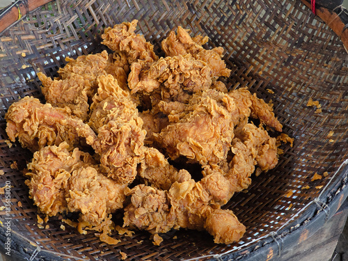 Freshly fried crispy chicken pieces resting on a bamboo strainer after cooking. crunchy textures and warm golden coloration