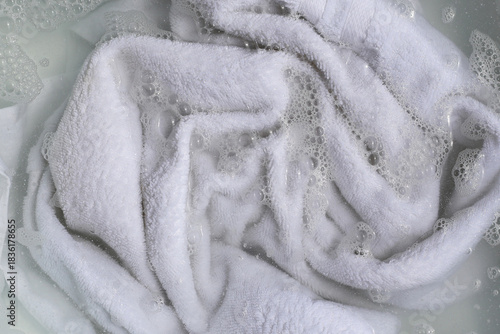 Bild auf Leinwand White towel soaking in a basin of soapy, bubbly water.