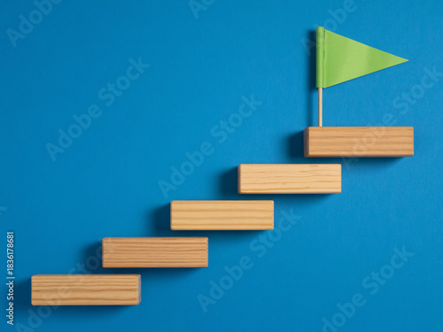 Ascend to success with building blocks leading to a vibrant green flag, symbolizing achievement and reaching goals.