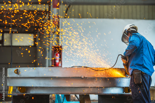 Worker using electric wheel grinding on steel structure in factory.