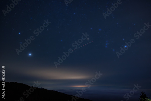 vista panoramica del cielo notturno stellato e parzialmente sereno, a inizio inverno, da un'alta quota in montagna, nel nord Italia, con nuvole che coprono le valli