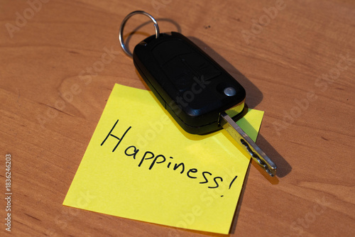 Hand written happiness on yellow sticky note , car key, conceptual first car image.