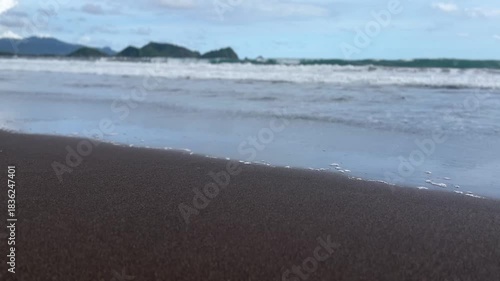Soft sea waves reach the dark shoreline with distant islands visible under a calm sky