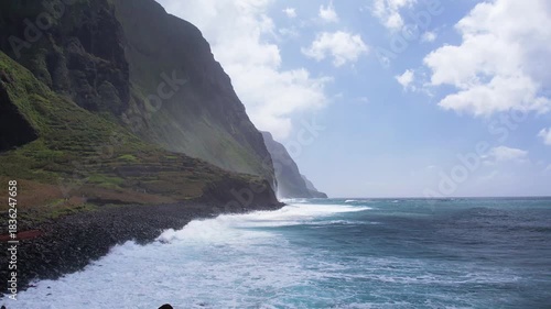 Majestic aerial view of Madeira's cliffs meeting the ocean. The towering rocky coastline covered in lush greenery creates a dramatic scene as waves crash against the cliffs below