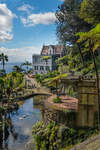 A serene garden scene in Madeira Monte Palace tropical garden in Funchal with lush greenery, a tranquil stream, and traditional architecture in the background. Ideal for nature lovers and tourists.