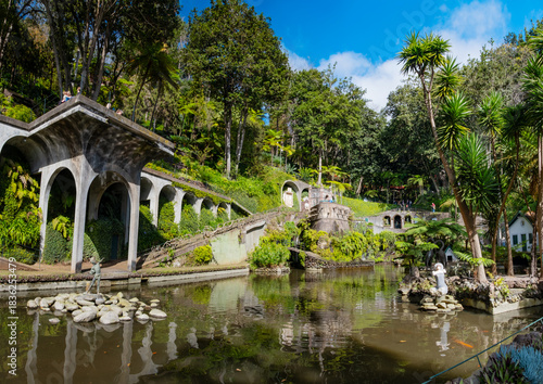 A serene garden scene in Madeira Monte Palace tropical garden in Funchal with lush greenery, a tranquil stream, and traditional architecture in the background. Ideal for nature lovers and tourists.