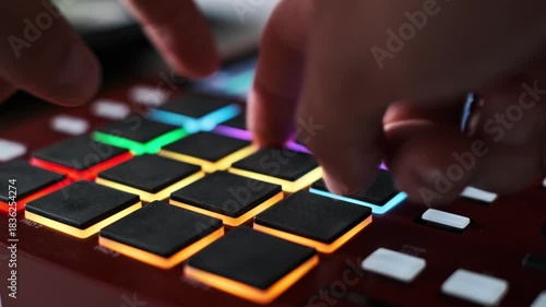 Extreme close-up shows musician's fingers rapidly playing a complex rhythm on a digital drum machine's multi-colored, illuminated pads in a professional audio recording studio environment.