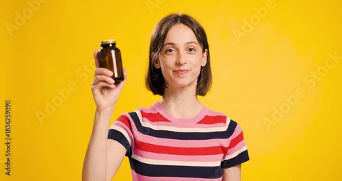 Young woman showcasing an empty brown pill bottle on a yellow background, displaying contentment