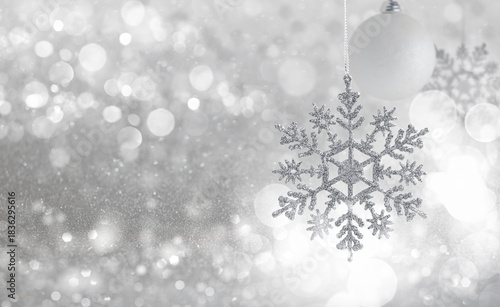 Sparkling Silver Snowflake and White Ornament on Glittering Winter Background. A delicate silver glitter snowflake ornament hanging near a matte white bauble against an ethereal, highly textured backg