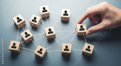 Hand places wooden block with a person icon, completing a connected network on a gray backdrop. Illustrates business connections, team building, and human resources concepts.