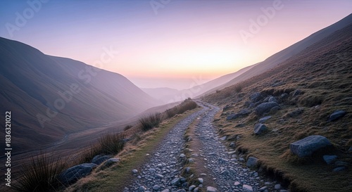 A scenic mountain path winds through a valley, bathed in the soft light of a sunset, creating a tranquil and atmospheric landscape.