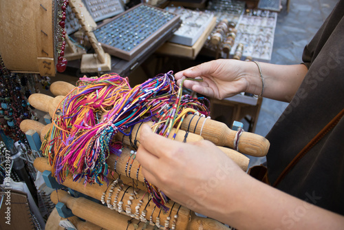 Female hands selecting colorful handmade thread bracelets on a wooden display, close view of craft jewelry in a shop, for fashion, retail, shopping, artisan craft, lifestyle, gift ideas.