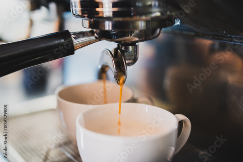 Espresso machine pouring fresh, hot coffee into two white cups, close-up shot. Barista prepares delicious cafe beverage in modern stainless steel commercial equipment