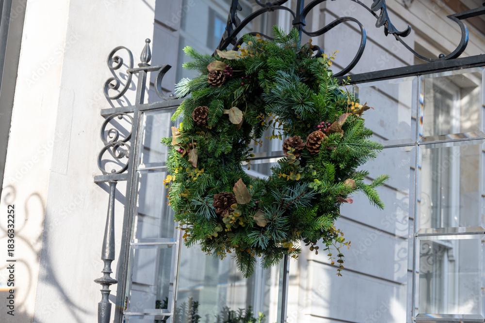 Fototapeta premium Festive Christmas wreath on window decorated with Christmas lighting, balls, Christmas trees with garlands, December holidays in England