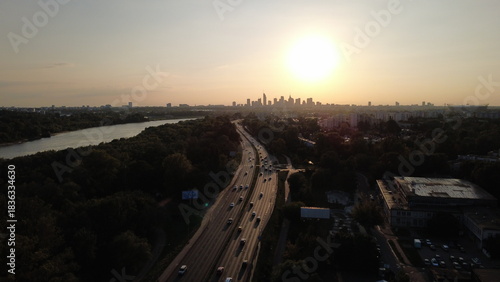 
Smooth drone footage flying toward the Warsaw city skyline during a warm summer sunset. The video captures the Vistula River, extensive green areas, residential neighborhoods, and a major highway fil