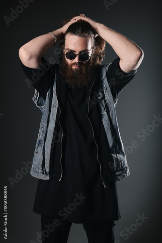 Studio fashion: handsome young man wearing jeans, denim coat and sunglasses (metalhead). Portrait of informal long-haired and bearded guy