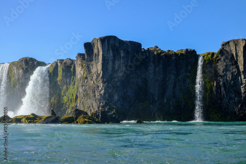 A view of a waterfall and rocky shore on a sunny day