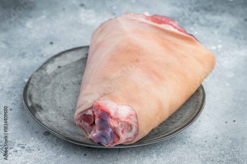 Raw pork knuckle hock showing rind surface, subcutaneous fat and exposed muscle tissues on stone plate with thyme for technical culinary visuals.