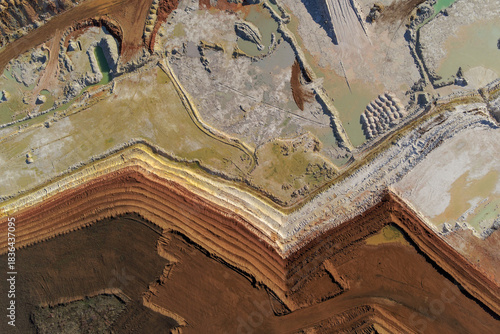 Top-down aerial view of a multi-colored industrial clay quarry with sharp zigzag layers of red, white, and brown earth, showing scale.
