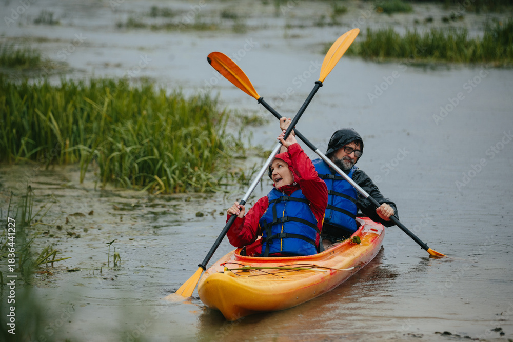 Fototapeta premium Senior couple kayaking in rain, embracing active lifestyle
