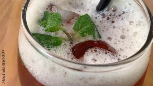 cold iced tea in a rounded glass, topped with foam and fresh mint, with a black straw. Inviting and casual, perfect for summer cafe or lifestyle imagery