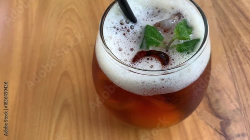 cold iced tea in a rounded glass, topped with foam and fresh mint, with a black straw. Inviting and casual, perfect for summer cafe or lifestyle imagery