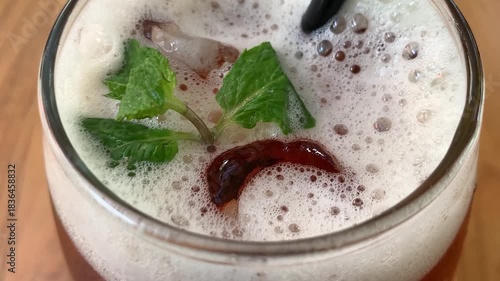 cold iced tea in a rounded glass, topped with foam and fresh mint, with a black straw. Inviting and casual, perfect for summer cafe or lifestyle imagery