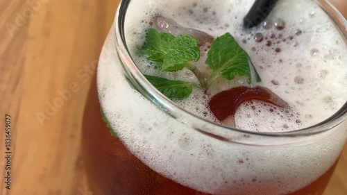 cold iced tea in a rounded glass, topped with foam and fresh mint, with a black straw. Inviting and casual, perfect for summer cafe or lifestyle imagery