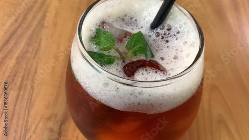 cold iced tea in a rounded glass, topped with foam and fresh mint, with a black straw. Inviting and casual, perfect for summer cafe or lifestyle imagery