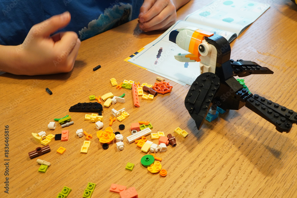 Obraz premium Child building a Lego toucan with instructions on a wooden table