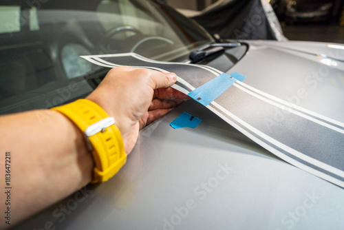 Worker installing car decals in garage, close-up of hand holding black vinyl film. Car decal application on hood.
