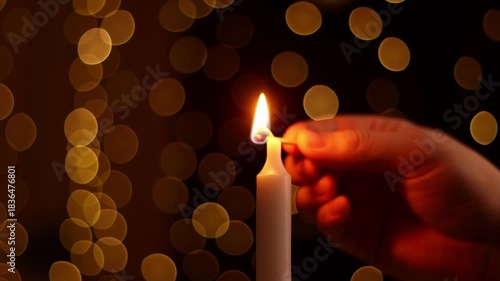 Close up of woman hand lighting red candle with a match surrounded by decoration with lights in background. Woman hands lighting advent candle with holly and fir branches. Girl burning red candle.

