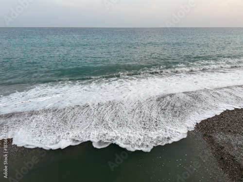Turquoise sea, waves rolling are onto the shore with white foam. Calm coastal scene perfect for travel, relaxation, and nature-themed projects