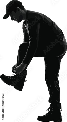 Silhouette of a young man wearing a cap and boots, bending over to tie his shoelace