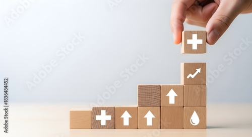 Hand stacking wooden blocks with growth chart, plus sign, and water drop icons for business success and healthcare