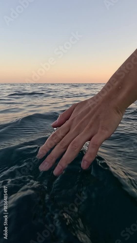Hand water ocean, gentle touching splashing calm sea at sunset. Vertical video.