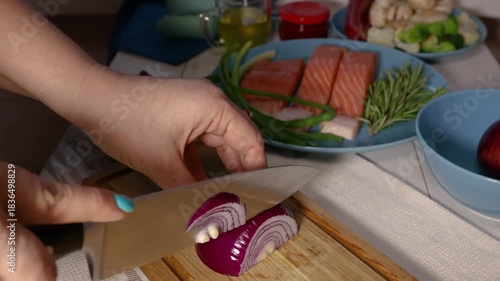 Woman's hands slicing red onion on wooden board