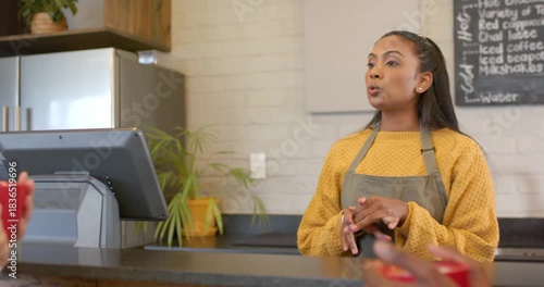 Receiving order Indian barista explaining menu at touchscreen counter, customer tasting in red mug