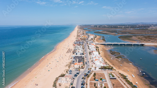 Aerial view shows Praia de Faro with its long sandy beach and the nearby Ria Formosa. People enjoy the beach while boats rest in the water