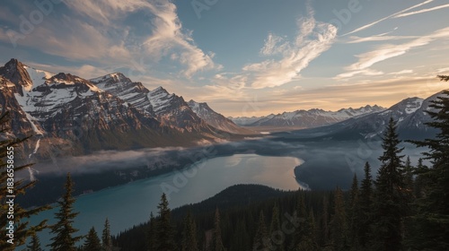 Aerial view of lake surrounded by mountains with snow capped peaks and a partly cloudy sky above it