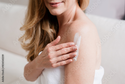 Woman applies moisturizer on her shoulder after a refreshing morning shower